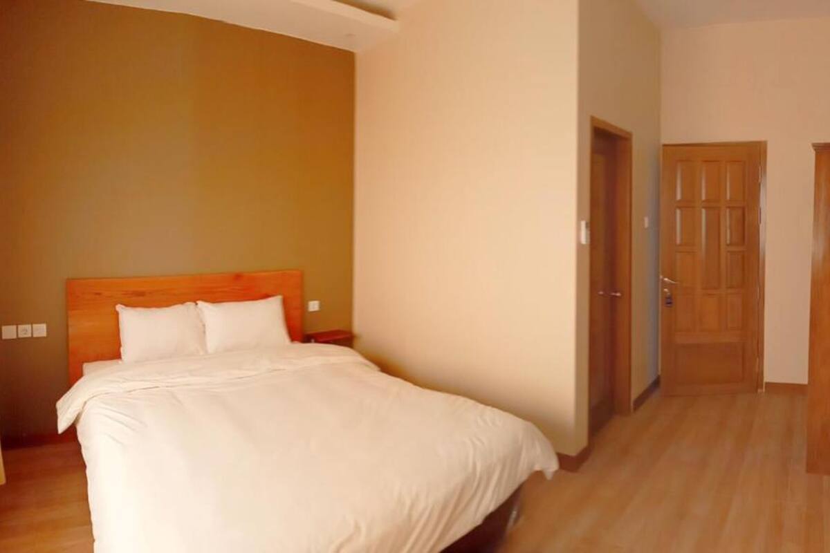 Camera d'albergo con un letto grande, una testiera e un pavimento in legno. Si vedono due porte e un cestino.