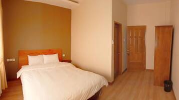 A hotel room with a large bed, wooden headboard, and a wooden floor. There are two doors and a trash bin visible.