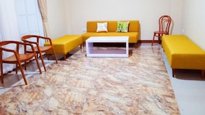 A room with a yellow sofa, two wooden chairs, a white coffee table, and a yellow bench. - Bluefire Homestay Syariah (Banyuwangi)