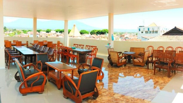 An outdoor seating area with tables and chairs, a tiled floor, and a view of buildings and greenery. - Bluefire Homestay Syariah (Banyuwangi)