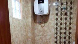 A small bathroom with a toilet, a wall-mounted water heater, and a shower area with patterned tiles. - Bluefire Homestay Syariah (Banyuwangi)