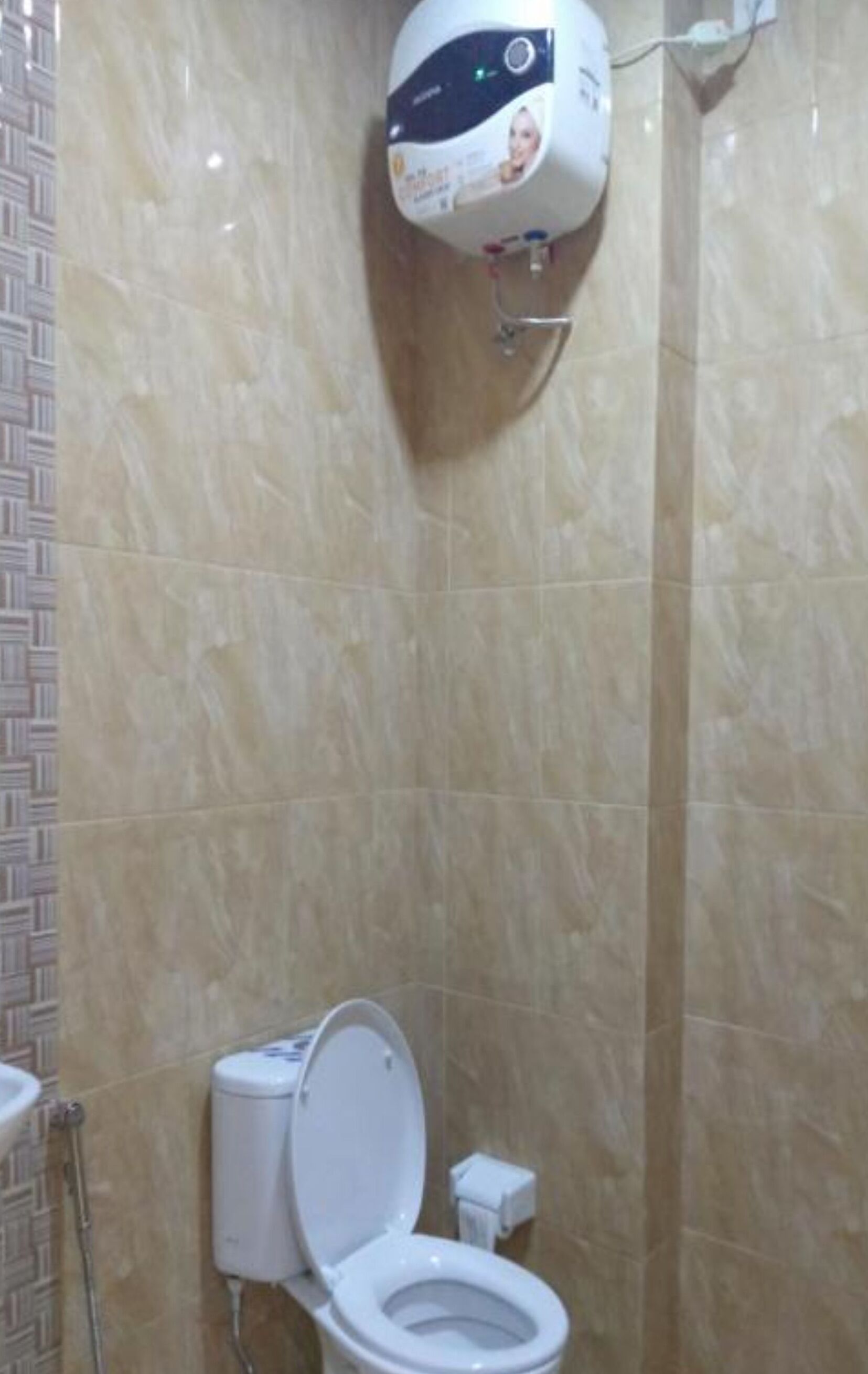 A bathroom with a toilet, a hand dryer, and a wall-mounted soap dispenser.