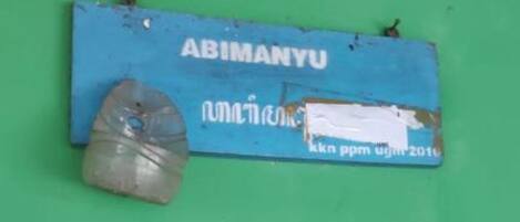 A blue sign with the text "ABIMANYU" and some other text in a different language, along with a plastic bottle on a green background.