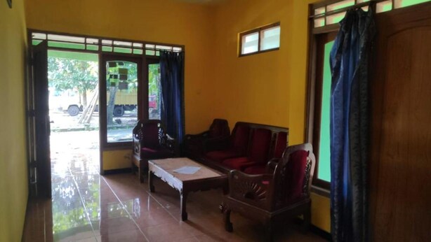 A room with a red sofa, a wooden coffee table, and a window with curtains. - Abimanyu Homestay (Imogiri)