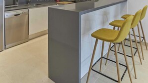Una cucina con forno a microonde integrato, lavastoviglie e angolo bar con sgabelli gialli.