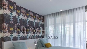 Camera da letto moderna con due letti, una parete decorata e un'ampia finestra con tende leggere.