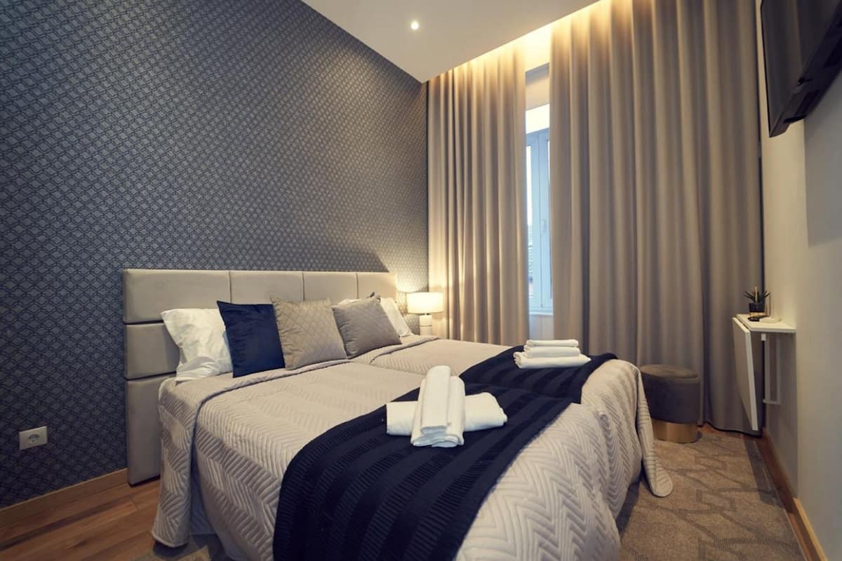 Ein modernes Hotelzimmer mit einem großen Bett, einem Nachttisch und einem Fenster mit Vorhängen.