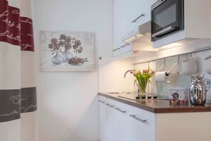 Une cuisine moderne avec des meubles blancs, un four à micro-ondes, une machine à café et un vase rempli de fleurs posé sur le comptoir.