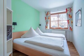 Ein Zimmer mit zwei Einzelbetten, einem Fenster mit floralem Vorhang, einem Heizkörper und einer Wandlampe.