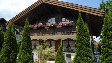 Ein traditionelles Chalet mit Holzbalkon, geschmückt mit Blumen, umgeben von hoch aufragenden Nadelbäumen.