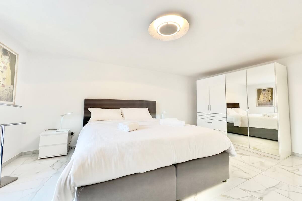 A modern bedroom with a large bed, bedside tables, a wardrobe, and a ceiling light.