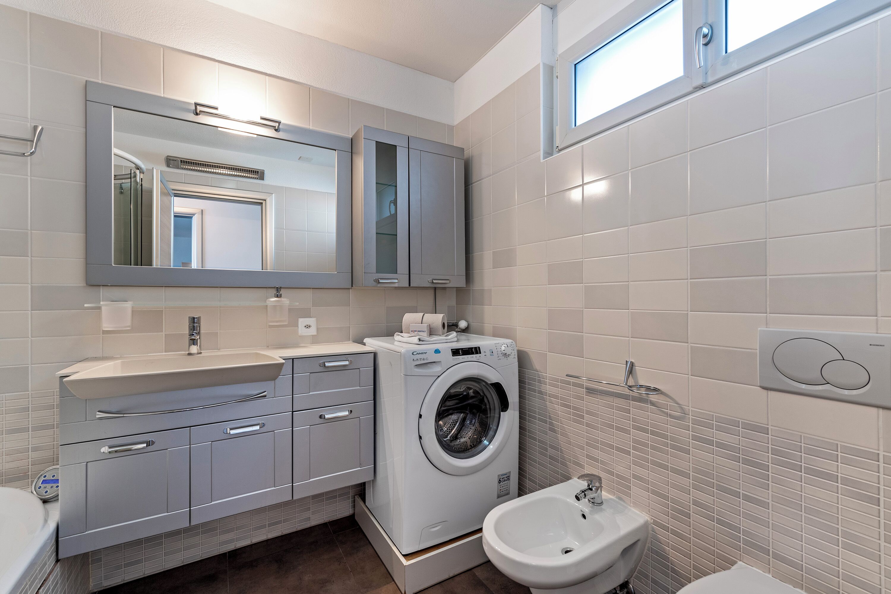A modern bathroom with a built-in washing machine, a bidet, and a large mirror.