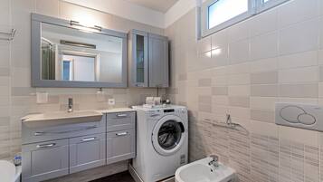 A modern bathroom with a built-in washing machine, a bidet, and a large mirror.