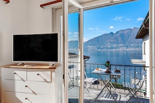A balcony with a TV, a table with a flower vase, and a view of a lake and mountains.