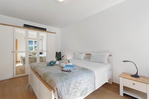 Un dormitorio con cama, mesita de noche, escritorio, armario y ventana.