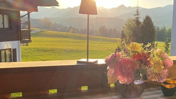 Un balcone con vista su un paesaggio montano, una lampada e un vaso di fiori.