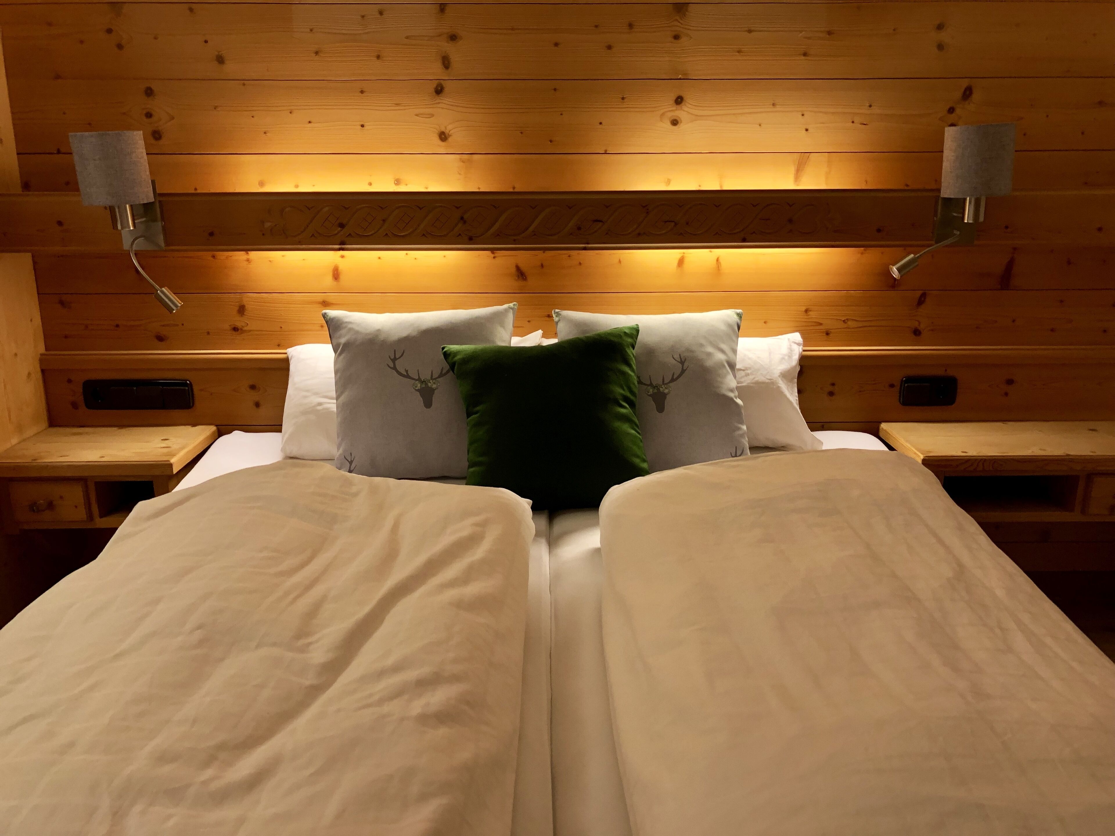 Un lit double avec deux oreillers, un vert et un blanc, dans une chambre aux murs en bois et dotée d’une tête de lit.