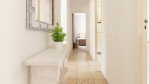 Un couloir étroit avec un banc blanc, une plante en pot et un lit visible au loin.
