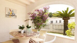 Une terrasse extérieure avec une table ronde et des chaises, entourée de plantes en pot et offrant une vue sur un quartier résidentiel.