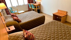 Una habitación de hotel con dos camas, una mesita pequeña, una silla y un escritorio con una lámpara.