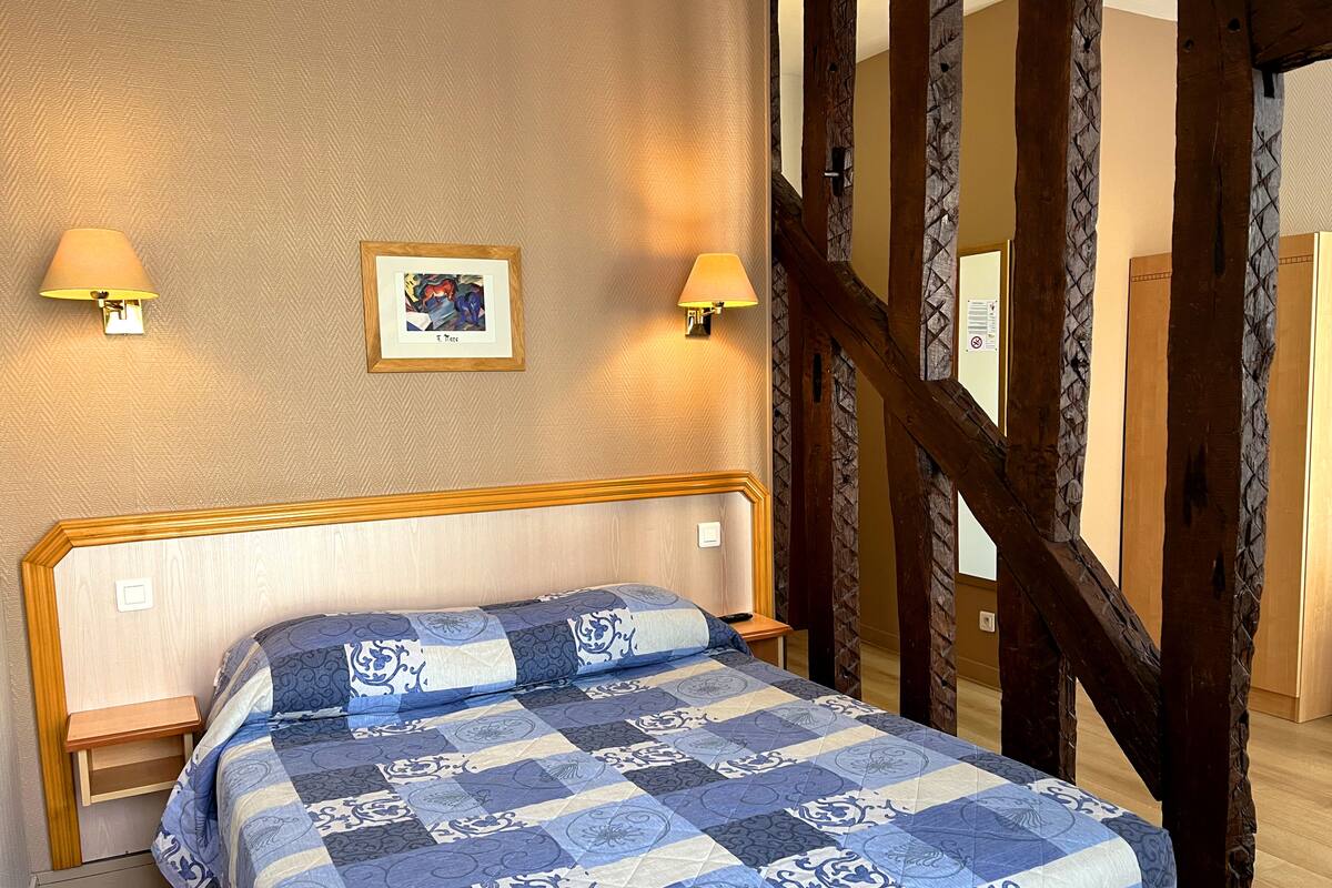 A bedroom with a bed, two bedside lamps, a framed picture on the wall, and exposed wooden beams.