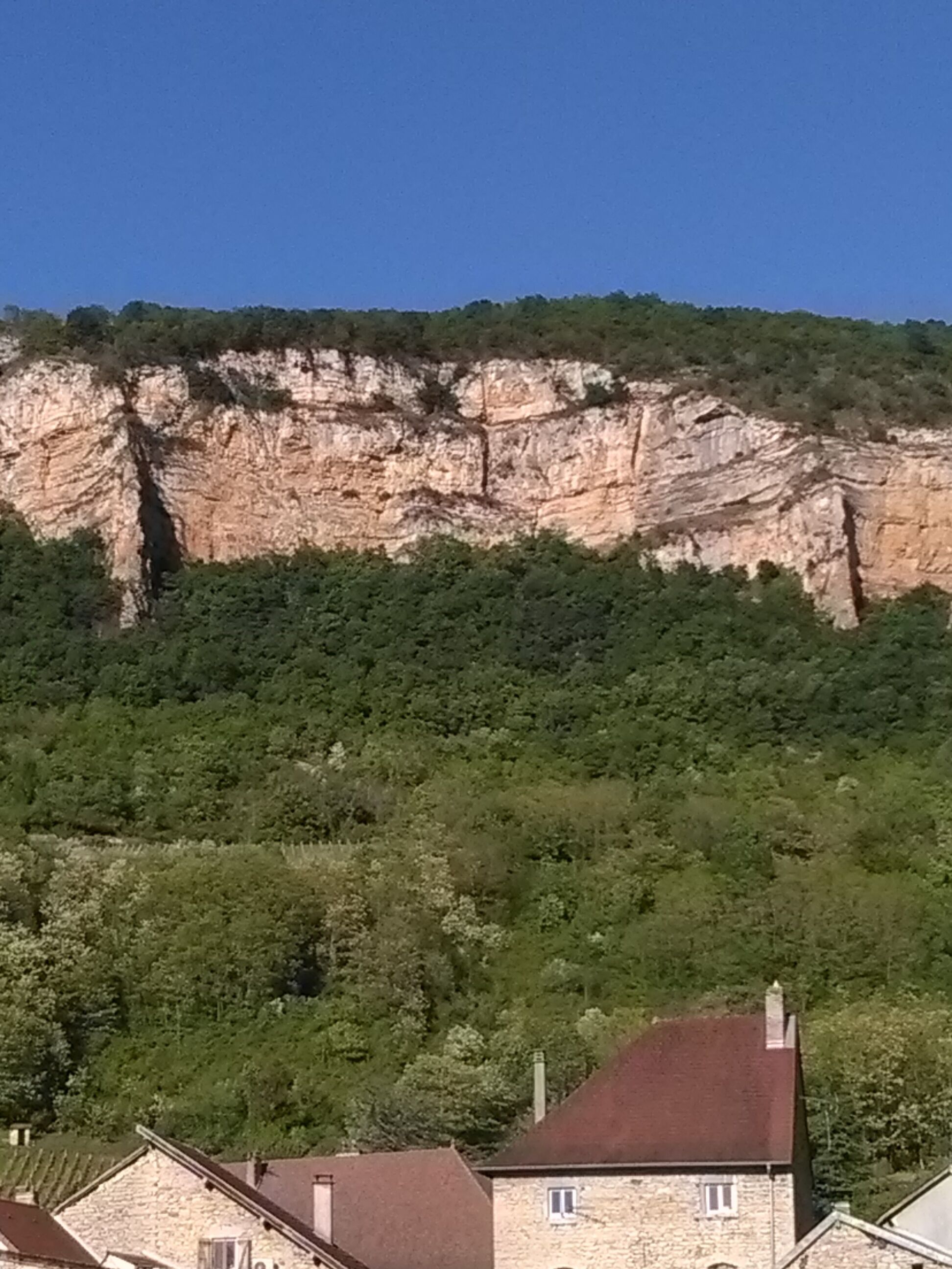 Un edificio in pietra con tetto rosso, circondato da alberi verdi e rigogliosi e da una scogliera con parete rocciosa.