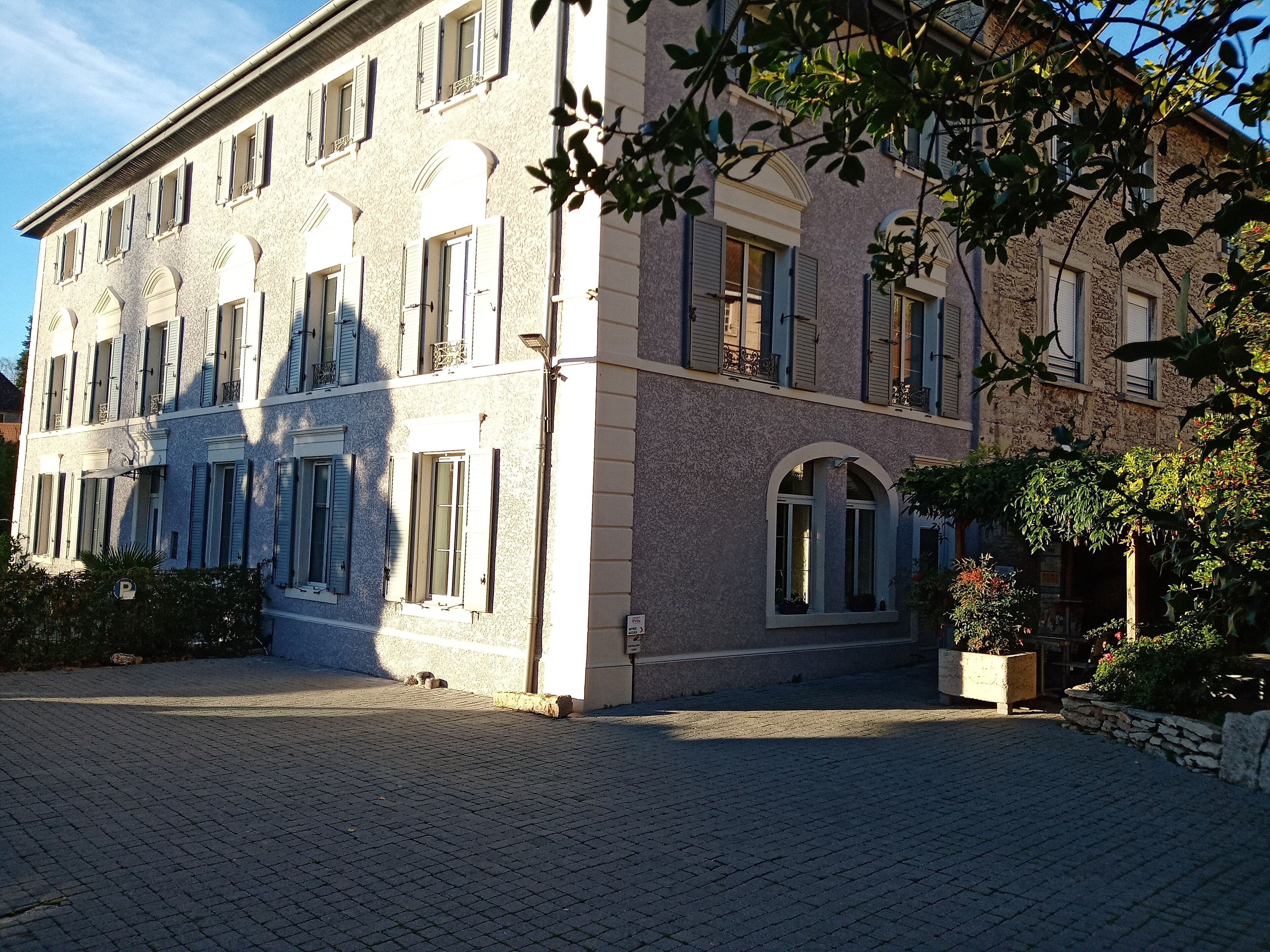 Un immeuble à plusieurs étages, doté d’une façade en pierre, de grandes fenêtres avec volets et d’une cour pavée.