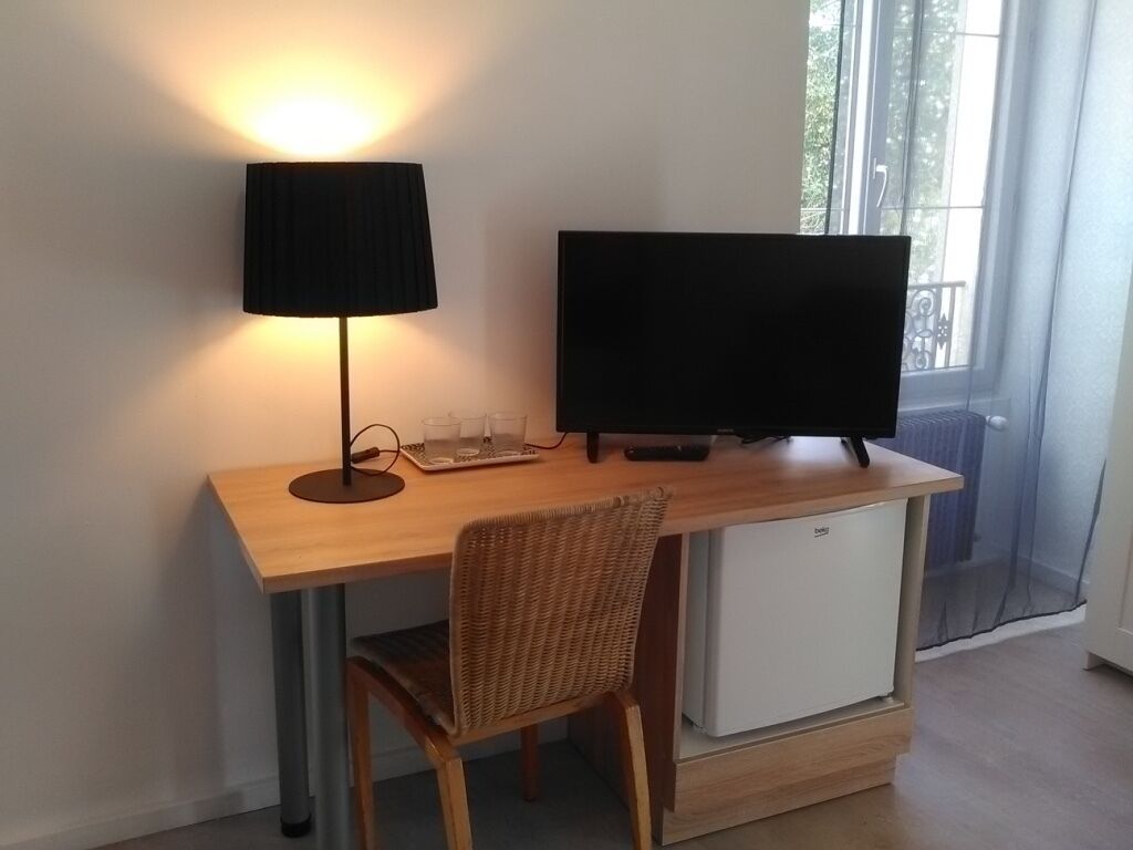 Un espace de travail compact comprenant un bureau, un écran d’ordinateur, une lampe et un petit réfrigérateur.