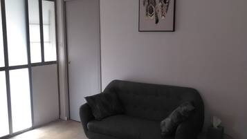 Une pièce avec un canapé gris foncé, une petite table ronde sur laquelle se trouve une boîte de mouchoirs, et une œuvre d’art accrochée au mur.