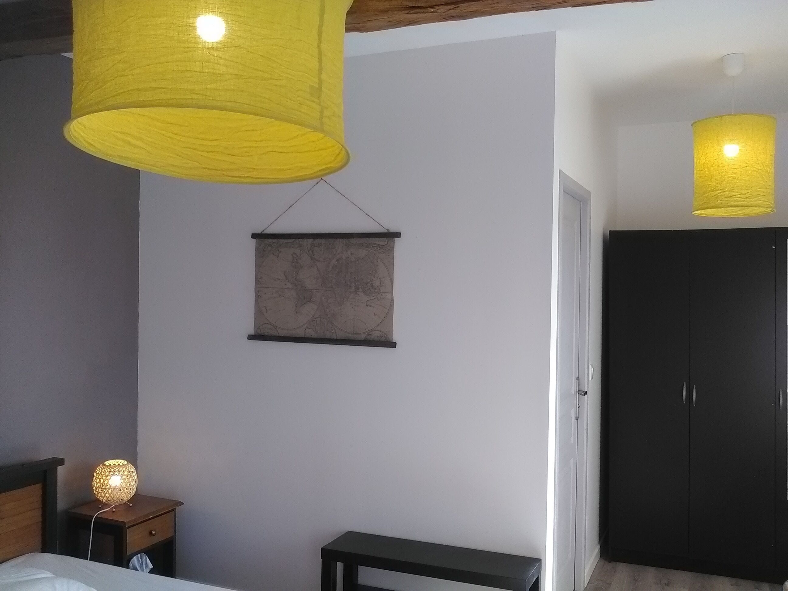 Une chambre à coucher avec un lit, une table de chevet avec une lampe, une carte accrochée au mur et une armoire.