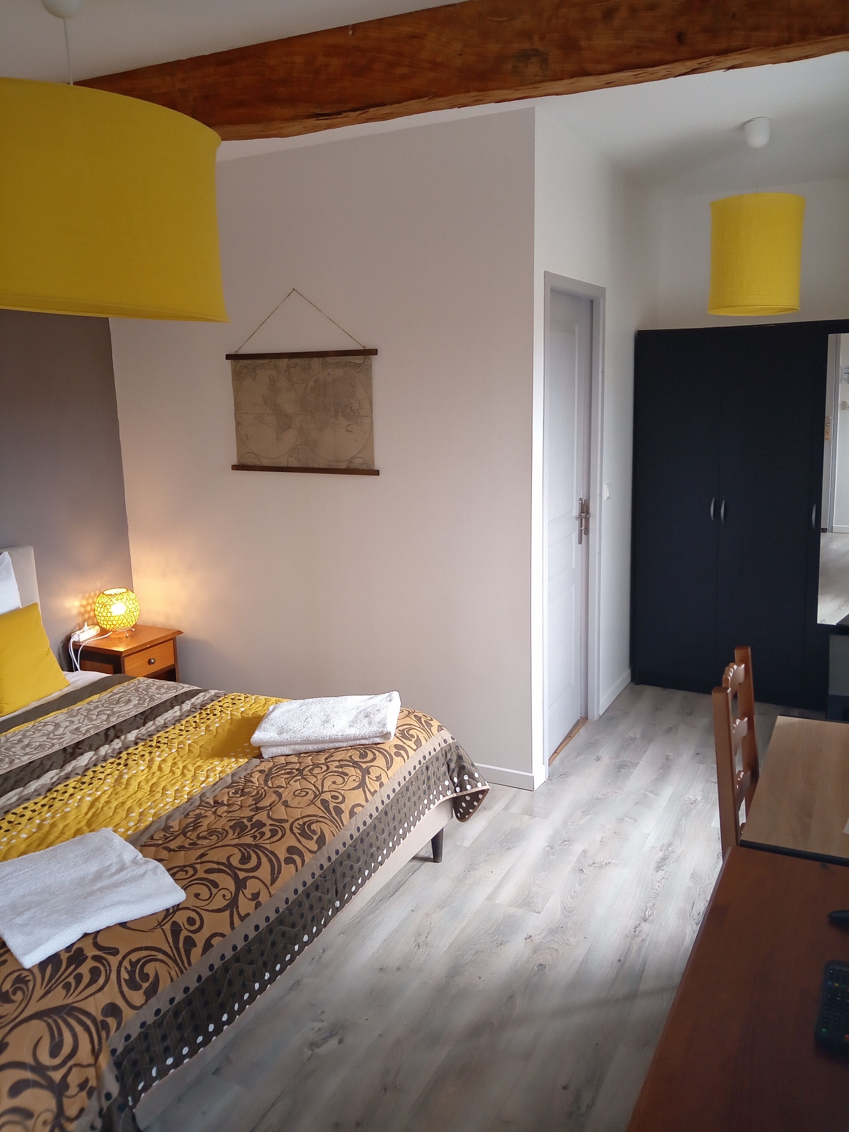 A bedroom with a bed, a wooden nightstand with a lamp, a map on the wall, and a wardrobe.