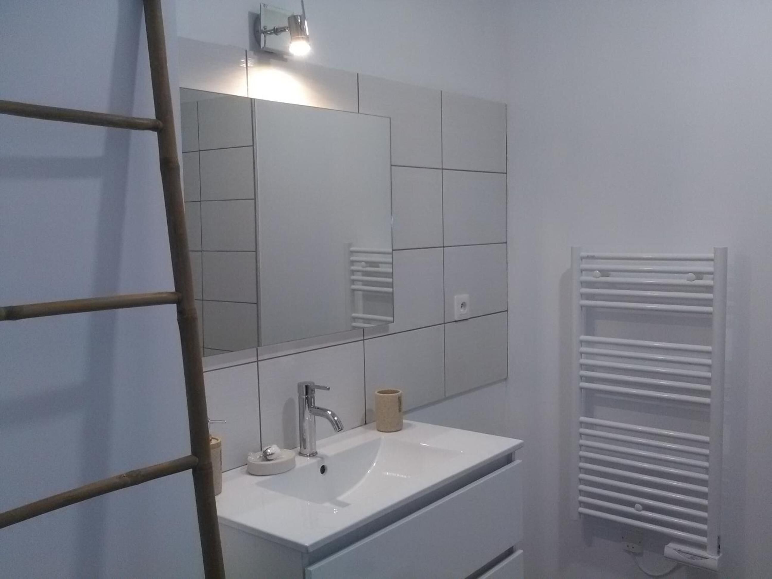 Un baño con lavamanos blanco, espejo y toallero.