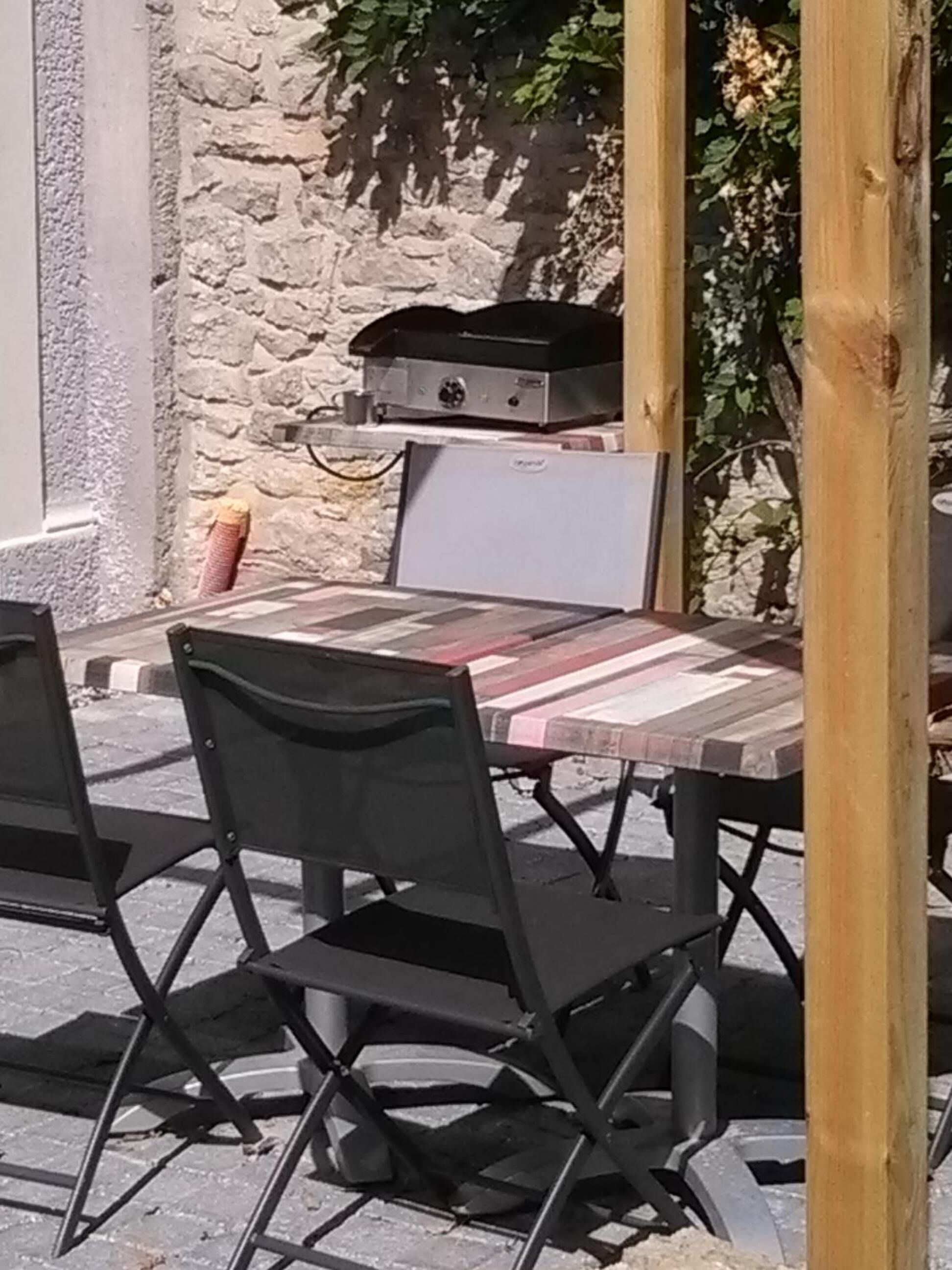 An outdoor dining area with a stone wall, a grill, and foldable chairs.