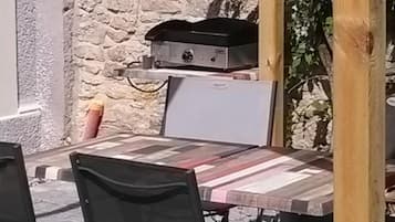 An outdoor dining area with a stone wall, a grill, and foldable chairs.