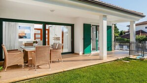 A covered patio area with a table and chairs, a green door, and a view of the surrounding neighborhood.