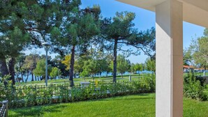 A view from a covered outdoor area with a grassy lawn, trees, and a distant body of water.