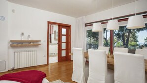 A modern living room with a sofa, a dining table with chairs, a red throw blanket, and a view of the outdoors through large windows.