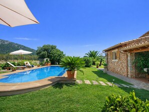 A swimming pool with lounge chairs, a stone building, and a grassy area with plants.