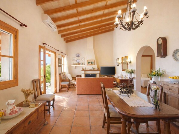 A spacious dining area with a wooden table and chairs, a kitchen in the background, and a chandelier.