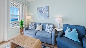A living room with a blue sofa, two side tables with lamps, a blue abstract painting, and a potted plant. - "Leeward I-7" | Beachfront Condo with Stunning Views of the Water | Bike to Seaside (Seagrove Beach)