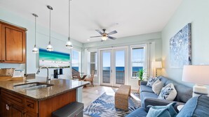 A spacious living area with a kitchen, a balcony with a view, and a ceiling fan. - "Leeward I-7" | Beachfront Condo with Stunning Views of the Water | Bike to Seaside (Seagrove Beach)