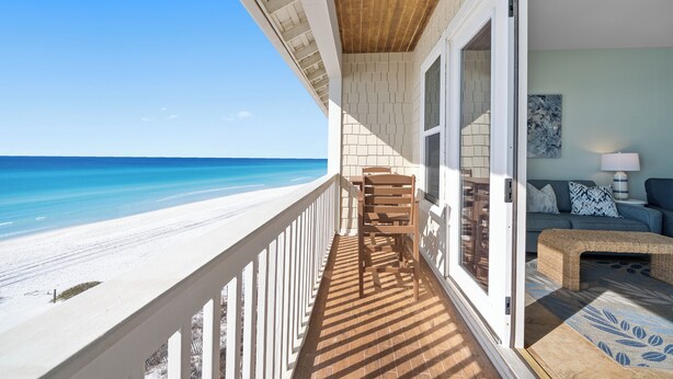 A balcony with a view of the beach, a wooden chair, a sofa, and a lamp. - "Leeward I-7" | Beachfront Condo with Stunning Views of the Water | Bike to Seaside (Seagrove Beach)