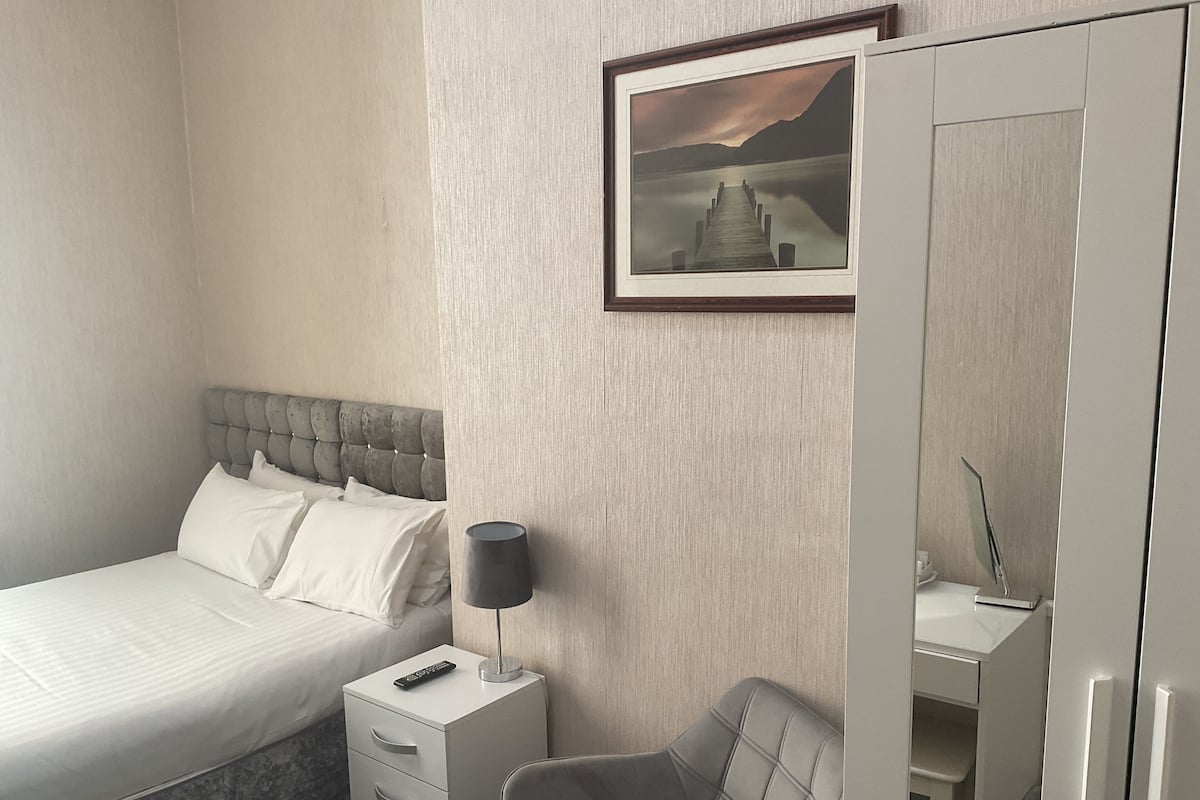 A hotel room with a bed, a bedside table with a lamp, a chair, and a wardrobe.