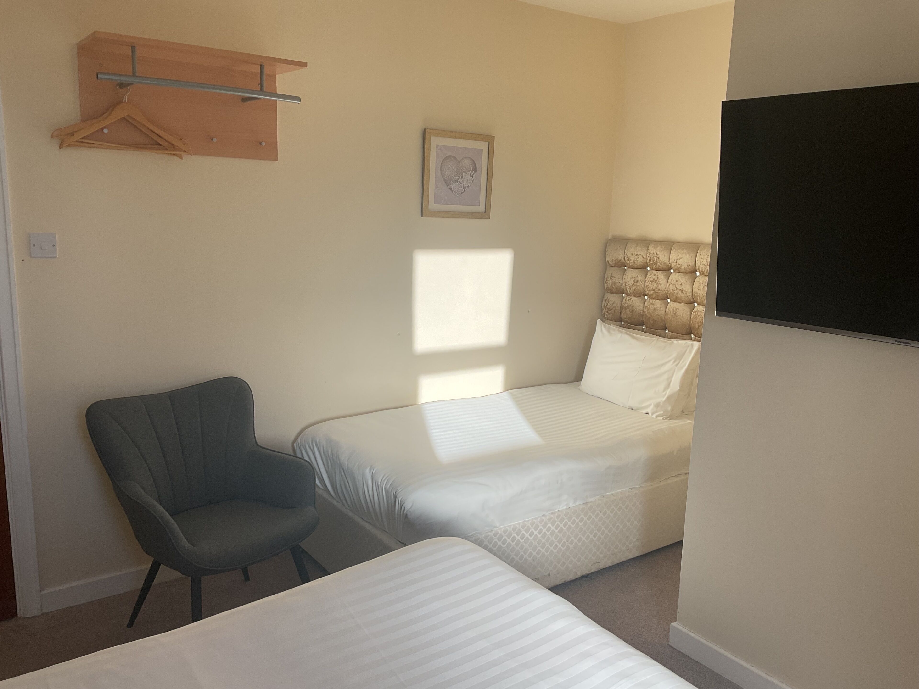 A bedroom with two beds, a chair, a wooden shelf, and a framed picture on the wall.