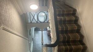 A staircase with a checkered carpet, white balusters, and a view of the ocean through a circular window. - Claremont Hotel (Preston)