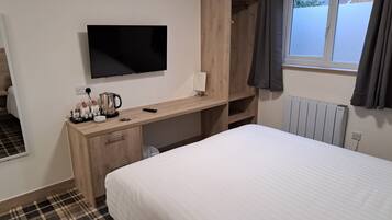 A hotel room with a bed, a desk with a TV, a radiator, and a window with curtains.