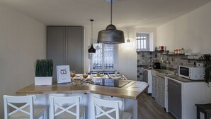 A modern kitchen with a central island, white chairs, a hanging light fixture, and a tiled backsplash. - Sapore di Sale by Wonderful Italy (Genoa)