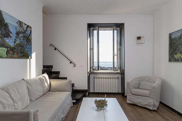 Una sala de estar con un sofá, una silla, una mesa de centro, una ventana con vistas y una escalera.