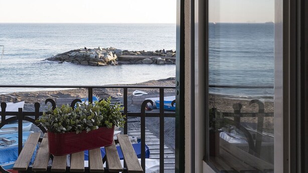 A view from a balcony overlooking a rocky shoreline with boats and a clear sky.