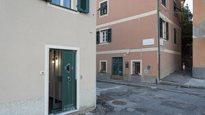 A narrow street with buildings on either side, featuring a green door and a white-framed window.